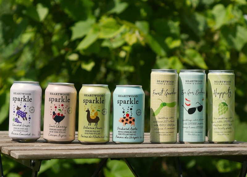 The Heartwood Sparkle and cider can lineup on a table outdoors