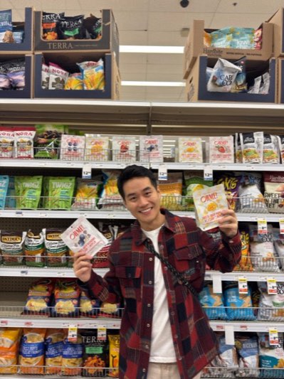 A person in a store snack aisle holding up two OHME! pouches