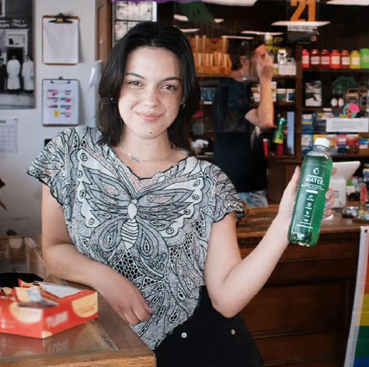 A shop worker holding a bottle of Chlorophyll Water at the counter of an independent store