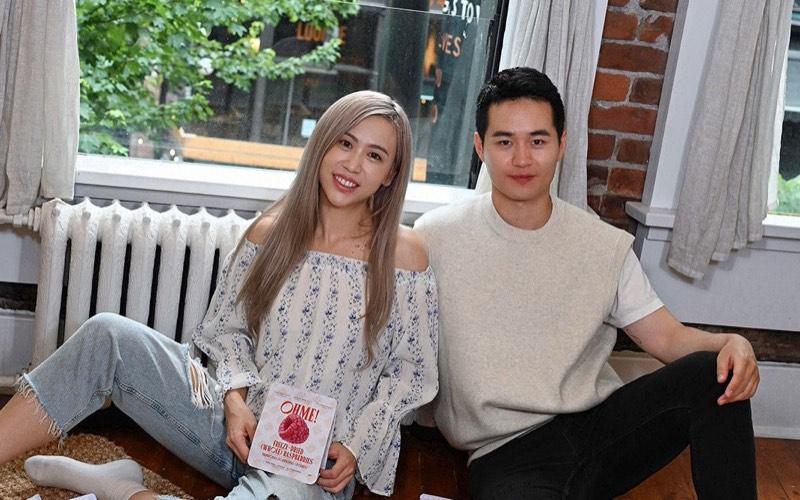 Two people sitting on the floor by a window, holding a pouch of OHME! freeze-dried raspberries