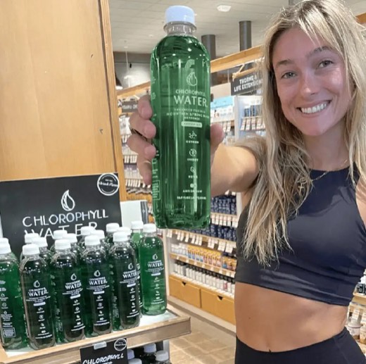 A shopper holding up a bottle of Chlorophyll Water beside an in-store display